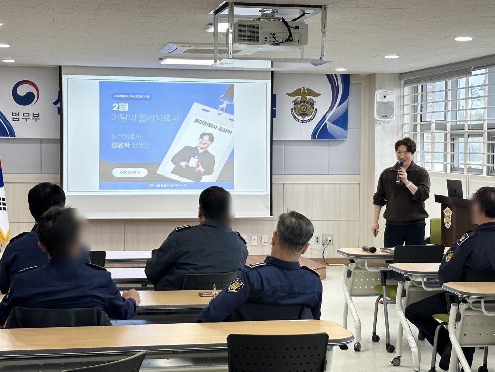 제복을 입은 직원들 앞에서 슬라이드를 띄우고 강의하는 장면