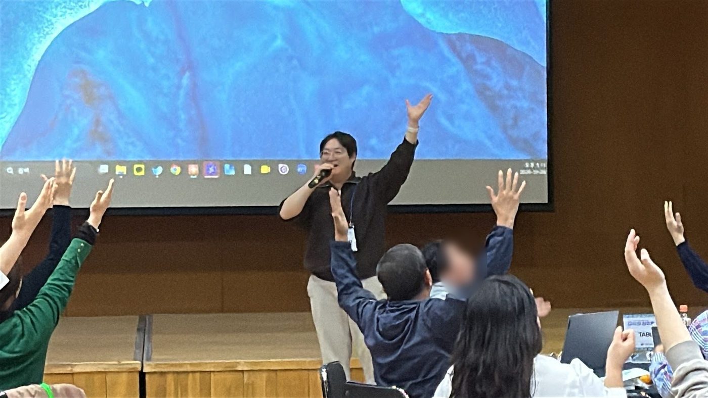 마이크를 들고 동작을 이끄는 강사와 두 팔을 올린 참가자들