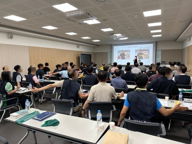 강의실을 가득 채운 임직원들이 자리에서 일어나 팔을 옆으로 뻗는 동작을 함께 하는 뒷모습