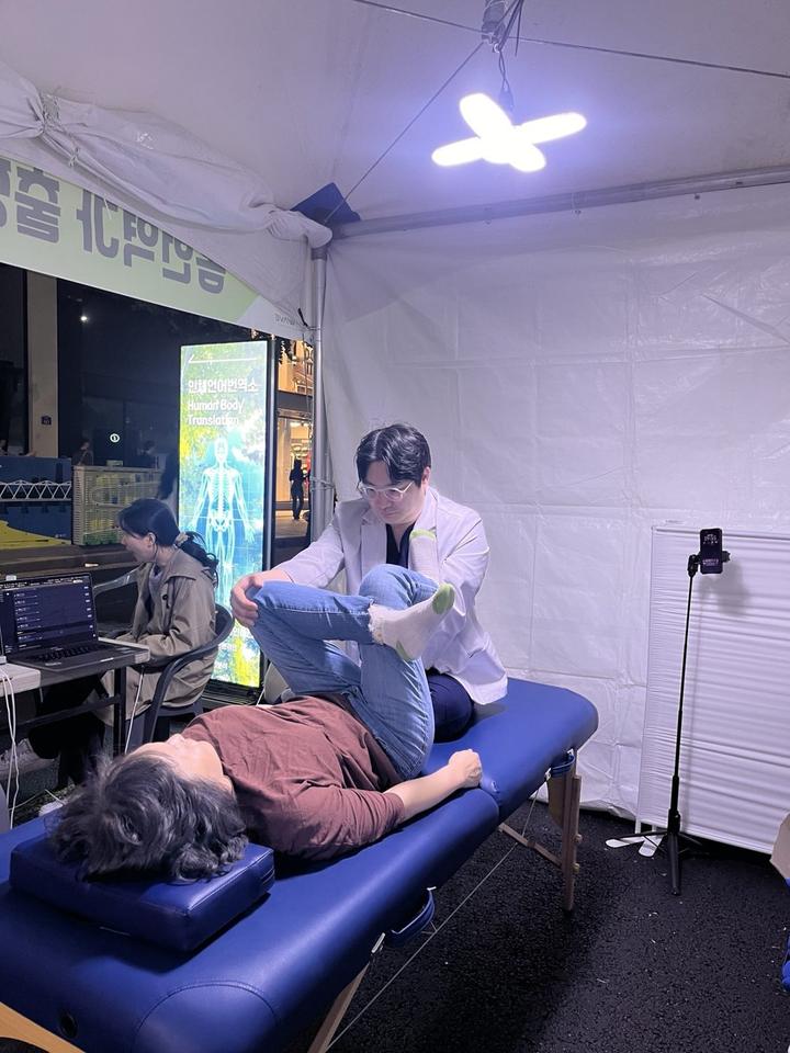 축제 부스 안에서 물리치료사 김윤하가 게스트의 움직임을 살피는 장면
