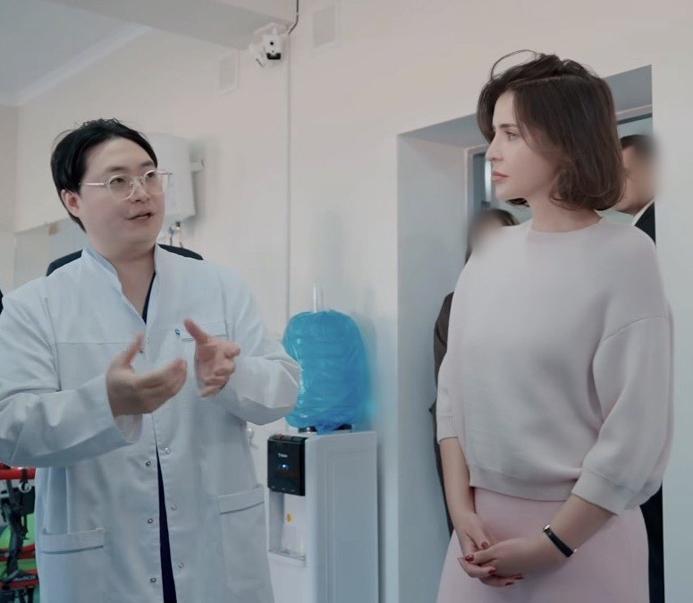흰 가운을 입은 물리치료사 김윤하가 우즈베키스탄 사회보호청 제1부청장에게 재활 현장을 설명하는 모습